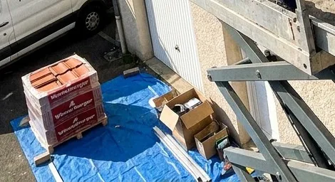 Tuiles neuves et cartons de matériel posés sur une bâche bleue au pied de la nacelle Rooflia, chantier de toiture à Massy